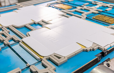 Der gestanzte Kartonage Zuschnitt mit Hochprägung liegt auf einer Marbach-Stanzform mit Prägeklischee | © Marbach Group